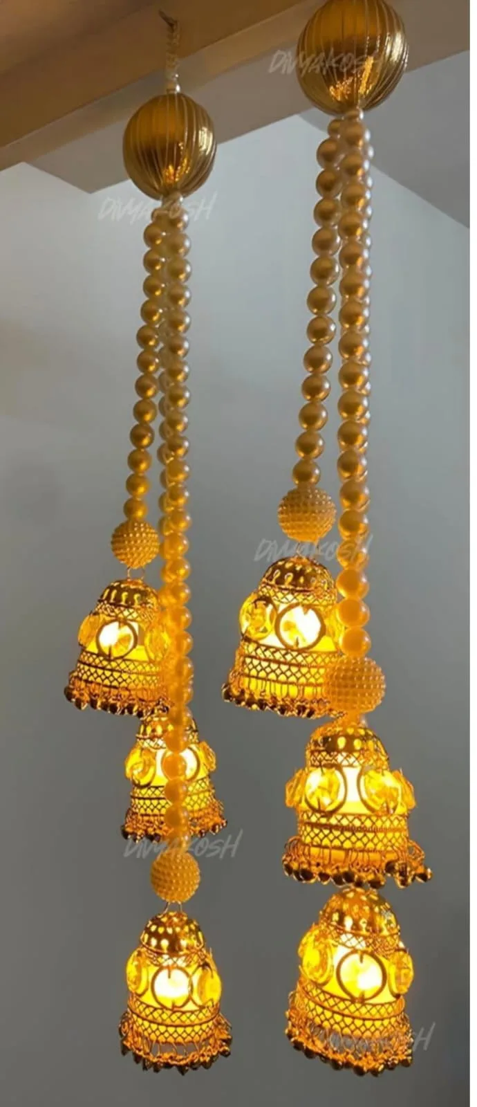 Jhumka Metal Hanging Lamp with Lights (Set of 2) | Youteek 1 Jhumka metal hanging lamp, set of 2. Golden finish with pearl strings, 3 battery-operated light strings in each. Cage about 4 inches, length about 19 inches. PVC box packing. golden jhumka lamp with pearl strings